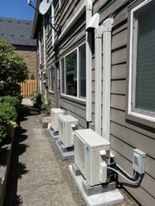Multiple outdoor heat pump units professionally installed along the side of a building by The Heat Pump Store in Portland, OR.