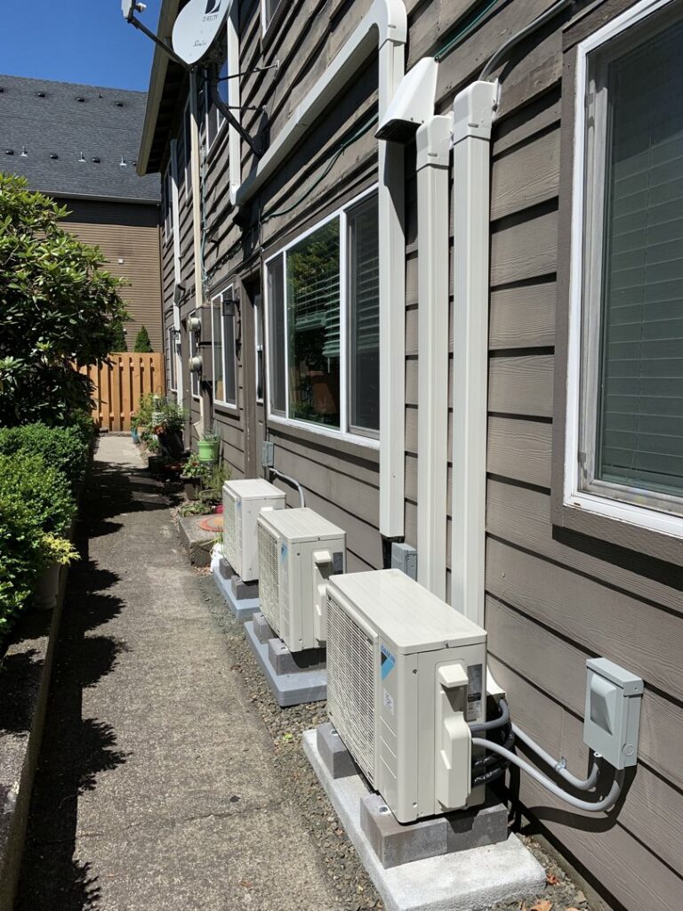 Multiple outdoor heat pump units professionally installed along the side of a building by The Heat Pump Store in Portland, OR.