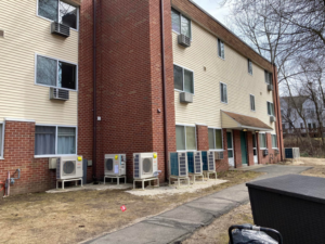 Multiple outdoor HVAC condenser units installed along the side of a commercial building by Express Plumbing in Hatfield, MA.