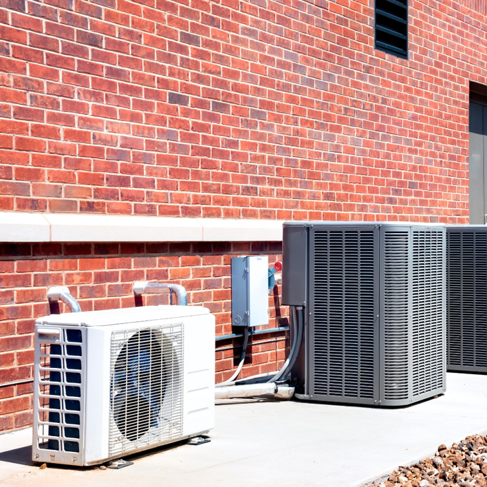 Multiple outdoor HVAC condenser units installed next to a brick building by M Heating & Cooling, Inc. in Green Bay, WI