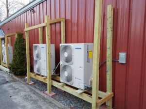 Multiple Samsung HVAC outdoor units installed on custom wooden frames next to a red building by Laird's HVAC in Auburn, ME.