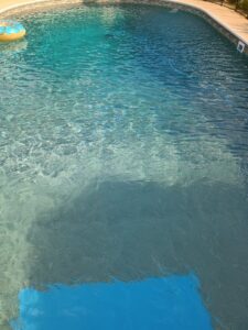 A murky pool with a pool vacuum hose, indicating cleaning is in progress or needed by Brian's Pool Service in Baton Rouge, LA.