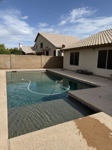 A swimming pool with slightly murky water and a cleaning hose, showing a pool being serviced by Brigade Pool Services in Tempe, AZ.