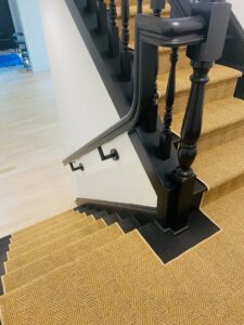 A natural fiber look carpet runner installed on a staircase with black banisters by Carpet Binding Company in Charlotte, NC.