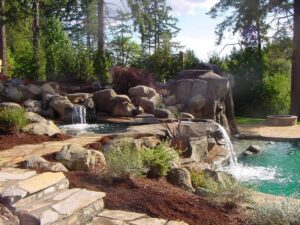 A natural-looking pool area with rock features, multiple waterfalls, and lush landscaping by Anderson Poolworks in Wilsonville, OR.