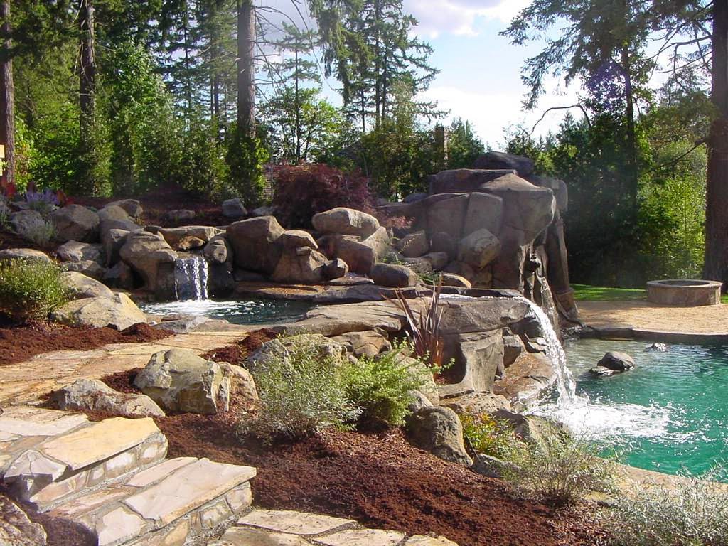 A natural-looking pool area with rock features, multiple waterfalls, and lush landscaping by Anderson Poolworks in Wilsonville, OR.