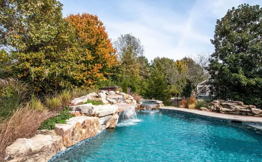 A swimming pool featuring a natural rock waterfall and lush landscaping by Top Tier Pools in Franklin, TN.