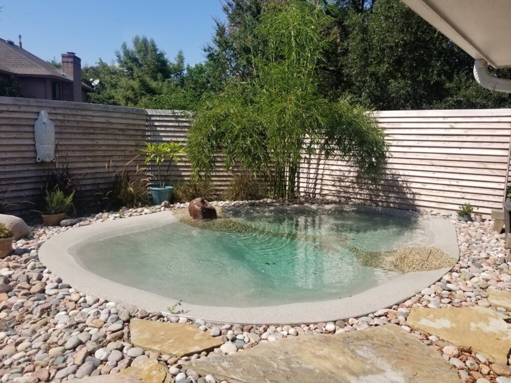 A natural-style small pool with a pebble surround and bamboo landscaping, a project by The Staycation Builders in Fort Wayne, IN.