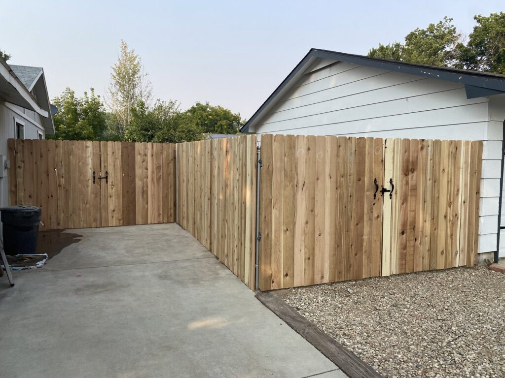 A natural wood privacy fence with two gates, creating an enclosed space next to a garage, by ZBros Fencing LLC in Boise, ID.