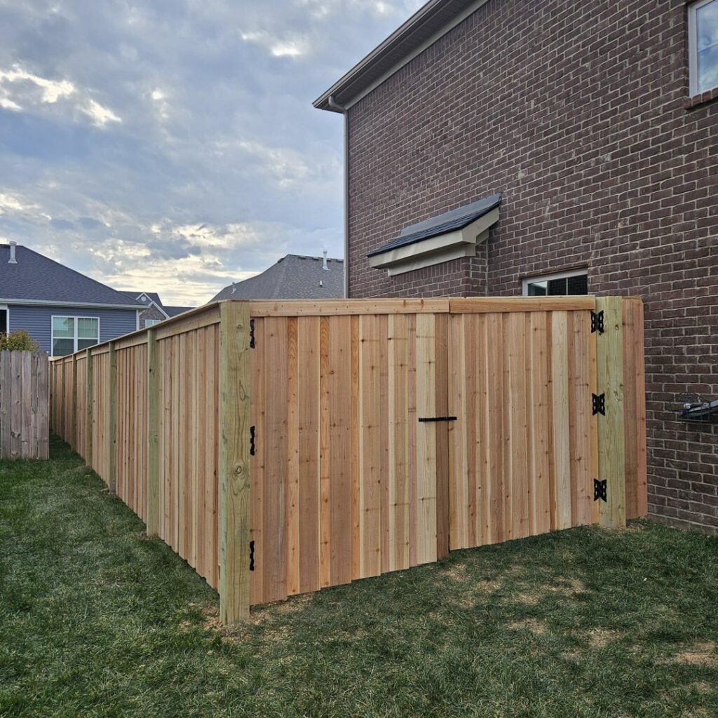 A new natural wood privacy fence with a gate installed next to a brick house by Border Built Fencing in Florence, KY.