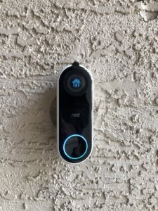 A Nest smart doorbell with a glowing blue ring, professionally installed on an exterior wall by PTech Installs in Columbus, GA.