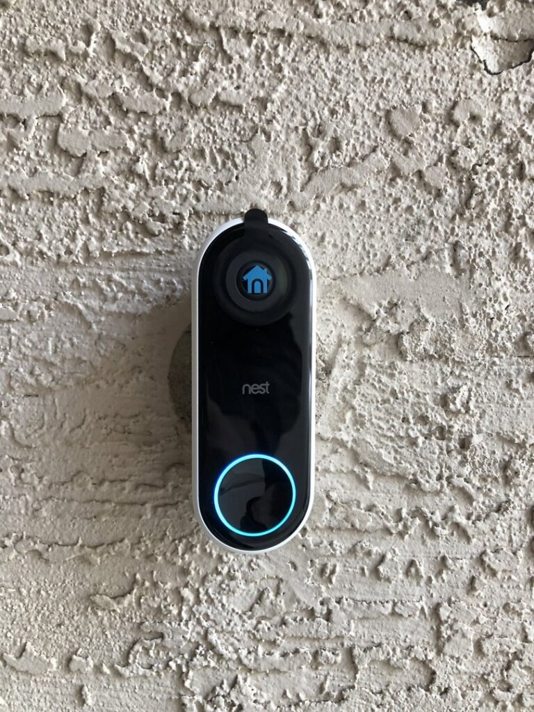 A Nest smart doorbell with a glowing blue ring, professionally installed on an exterior wall by PTech Installs in Columbus, GA.