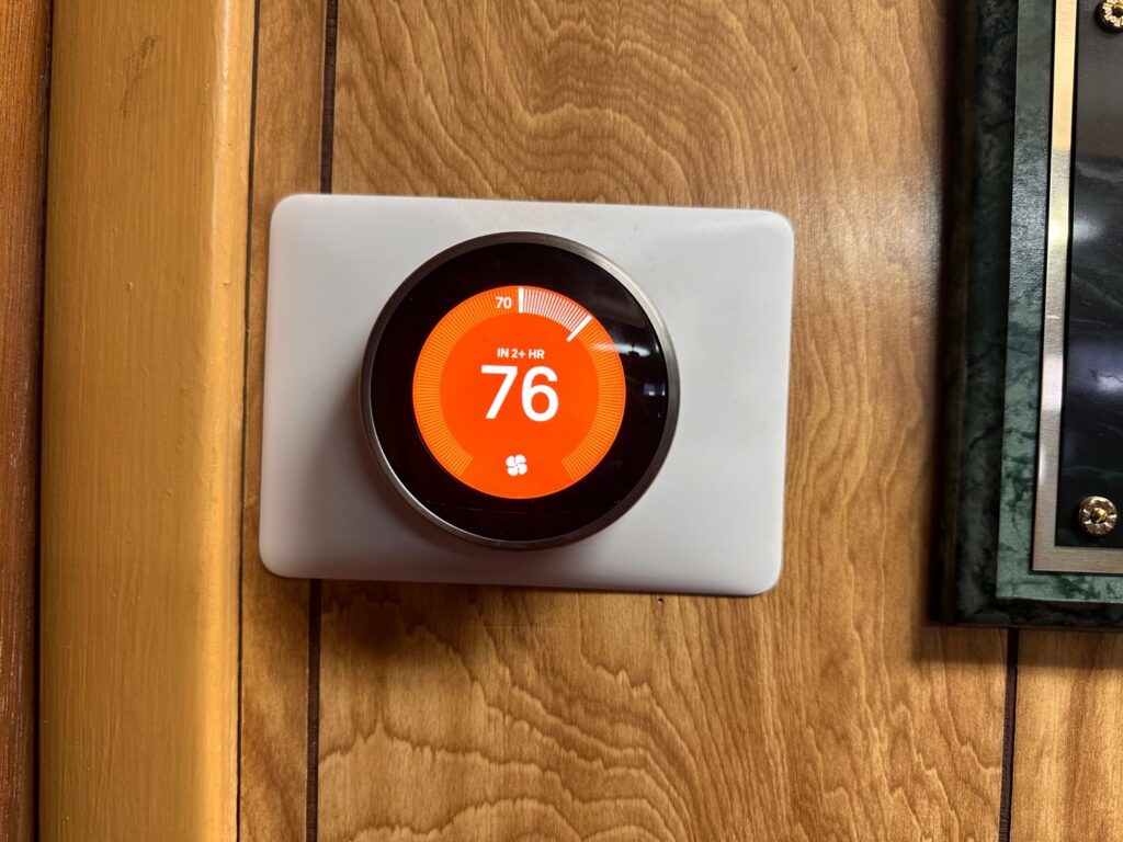 A Nest smart thermostat installed on a wooden wall by Metro Air Conditioning, Heating & Services in Dallas, TX