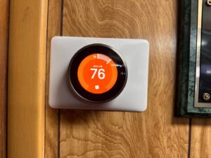 A Nest smart thermostat installed on a wooden wall by Metro Air Conditioning, Heating & Services in Dallas, TX