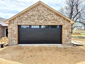 A newly installed black garage door with windows on a brick garage by APEX Garage Doors and Carports in Lawton, OK.