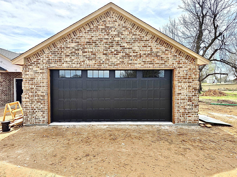 A newly installed black garage door with windows on a brick garage by APEX Garage Doors and Carports in Lawton, OK.