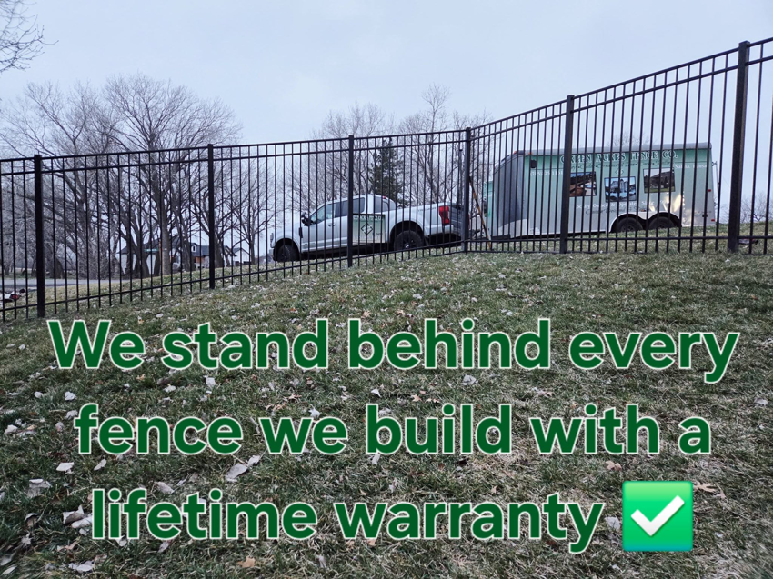 A newly installed black metal fence on a hill by Green Acres Fence Co in Salina, KS, with their truck and trailer visible.