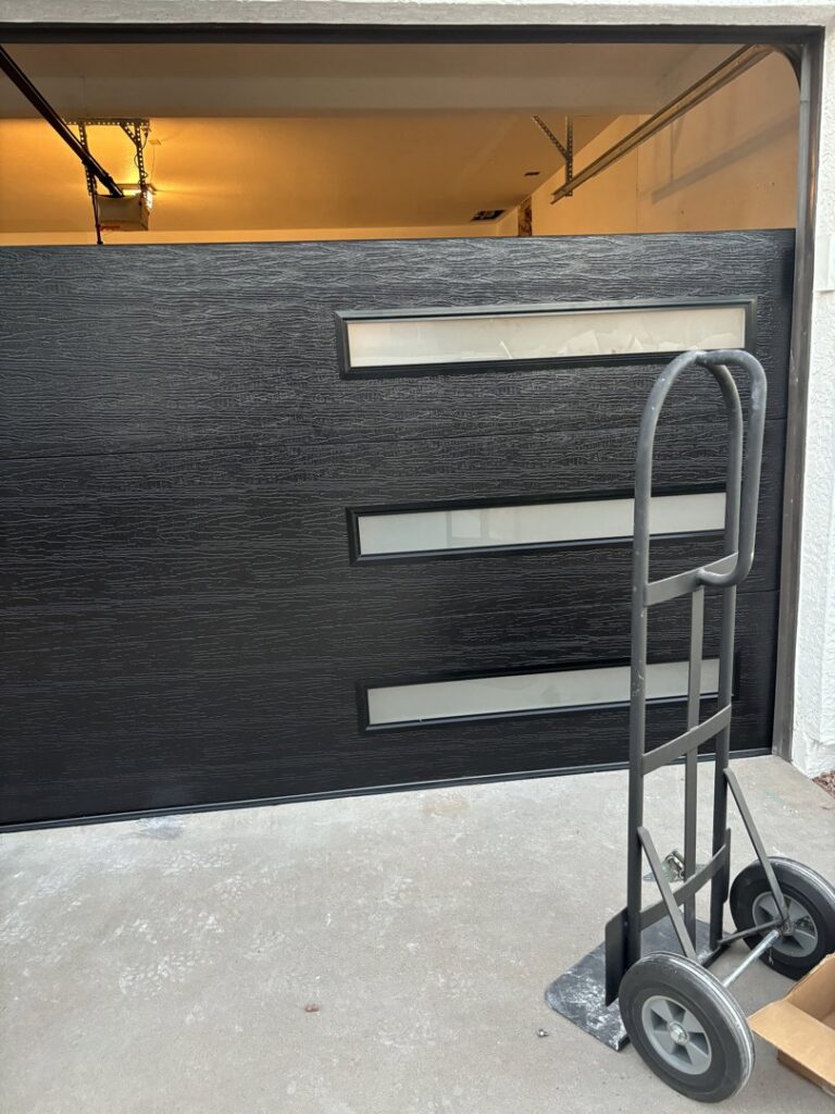 A new black modern garage door with horizontal windows being moved on a hand truck for installation by 101 Garage Doors in Phoenix, AZ.