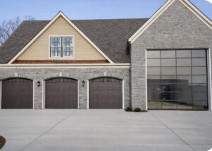 Newly installed brown panel garage doors and a modern glass garage door on a stone house by PRO-Line Garage Doors LLC in Richmond, KY.
