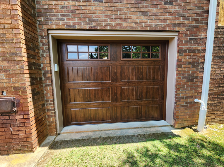 A newly installed brown garage door with decorative windows on a brick home by Getsinger's Overhead Doors in Spartanburg, SC.