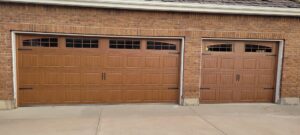 Two newly installed brown garage doors with windows on a brick house by Your Other Front Door LLC in Lakewood, CO.