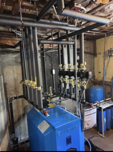A new blue Buderus boiler system with insulated black piping and valves, installed by HomeStyle Heating and Air LLC in Barrington, NH.