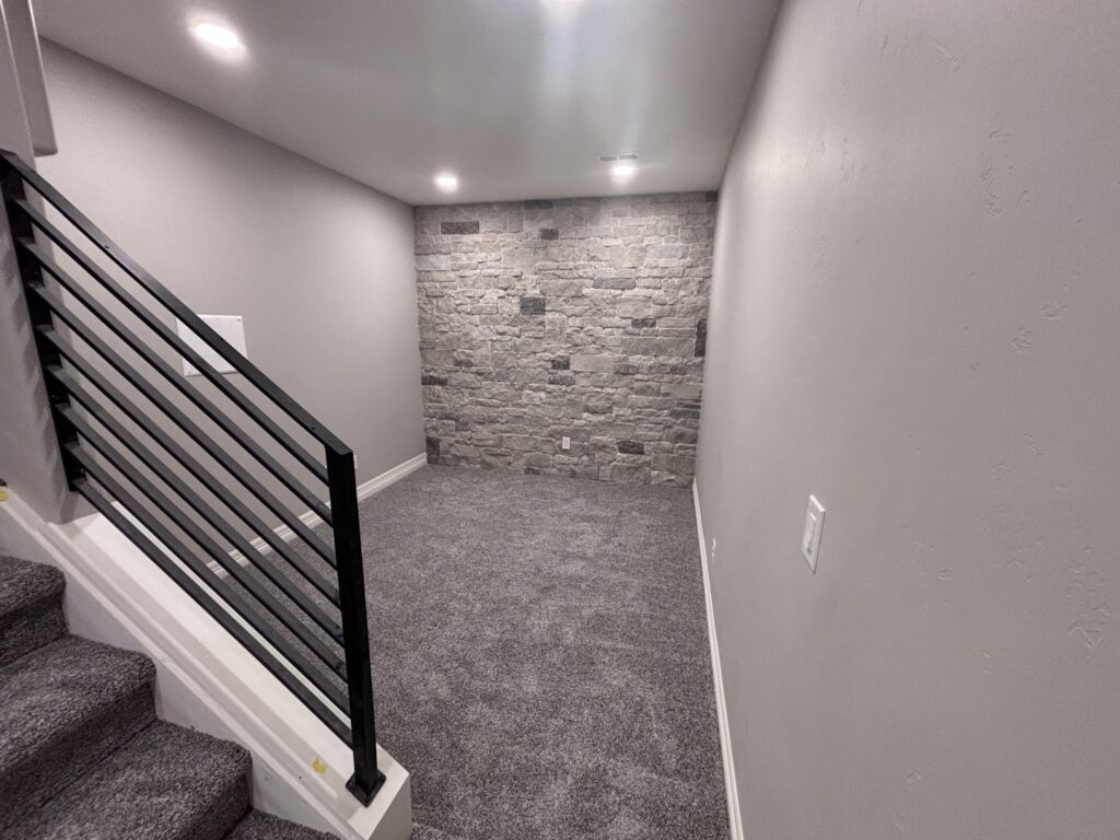 A newly installed carpet in a basement room with a stone accent wall by Carpet Direct of Northern Colorado in Loveland, CO.