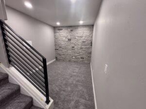 A newly installed carpet in a basement room with a stone accent wall by Carpet Direct of Northern Colorado in Loveland, CO.