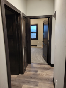 Newly installed carpet in a bedroom, visible from a hallway with wood-look flooring, by SchuhLess Flooring and Remodeling, LLC in Appleton, WI.