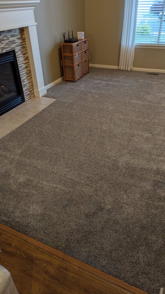 A newly installed carpet in a living room with a fireplace by Carpet Direct of Northern Colorado in Loveland, CO.