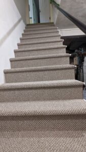 A newly installed light brown carpet on a staircase by National Carpet and Flooring in Tyngsboro, MA.