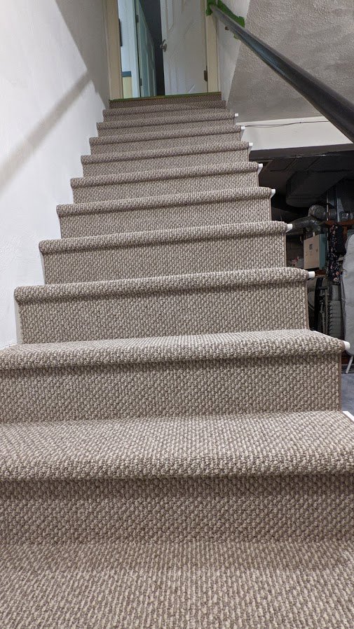 A newly installed light brown carpet on a staircase by National Carpet and Flooring in Tyngsboro, MA.