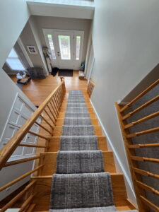 A newly installed grey carpet runner on a wooden staircase by Carpets Direct Naperville, IL.
