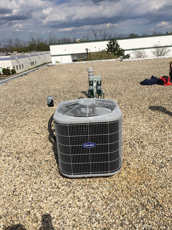 A new Carrier brand outdoor HVAC condenser unit installed on a gravel rooftop by Corbe Heating and Air Conditioning in Elgin, IL.