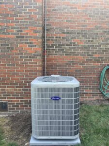 A newly installed Carrier outdoor HVAC unit against a brick wall by Delgado Enterprises in Pittsburgh, PA