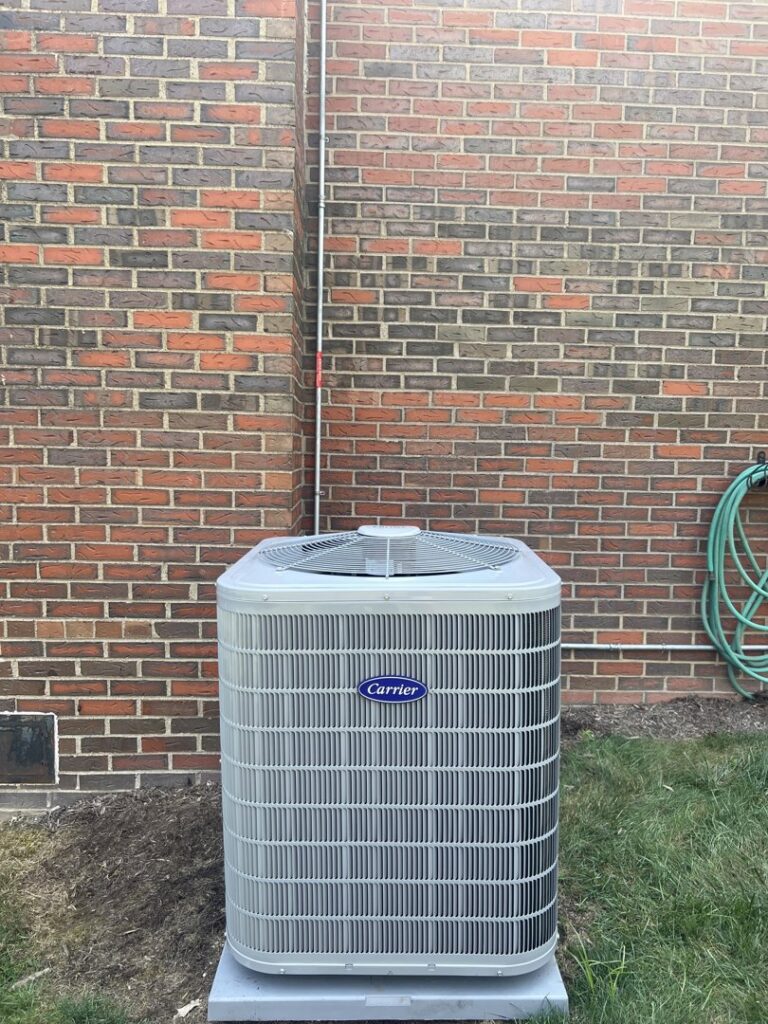 A newly installed Carrier outdoor HVAC unit against a brick wall by Delgado Enterprises in Pittsburgh, PA
