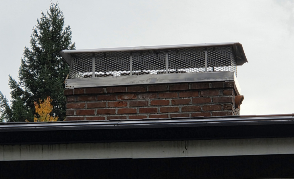 A newly installed metal chimney cap on a brick chimney by Matchbox Chimney Sweeps in Vancouver, WA.