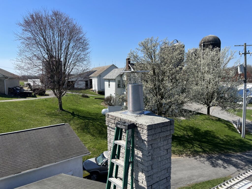 A newly installed stainless steel chimney cap and liner, with a ladder, by Maximum Energy Savers in Philadelphia, PA