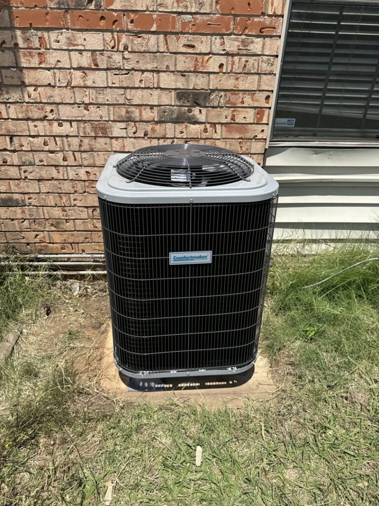 A new Comfortmaker AC unit installed on a concrete pad in a residential yard by Rhino Heating and Air Conditioning LLC in Norman, OK.