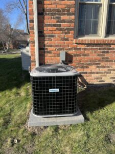 A new Comfortmaker AC unit installed on a concrete pad next to a brick house by Motown Mechanical Heating And Cooling in Westland, MI.
