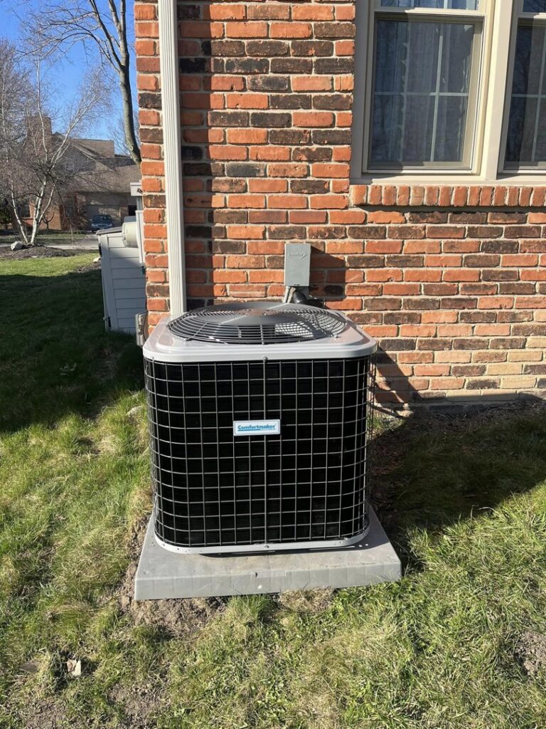 A new Comfortmaker AC unit installed on a concrete pad next to a brick house by Motown Mechanical Heating And Cooling in Westland, MI.