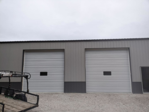 Two newly installed commercial garage doors on a grey building by Horton & Hill Garage Door Specialists LLC in Sapulpa, OK.