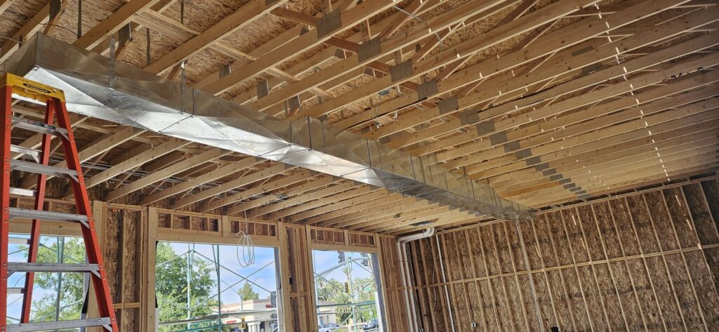 Large metal ductwork being installed in a new construction building with exposed wooden framing by HoxAir Heating & Cooling in Phoenix, AZ