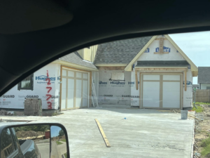 New construction garage door installation with white panels and wood trim by L & S Overhead Door in Tulsa, OK.