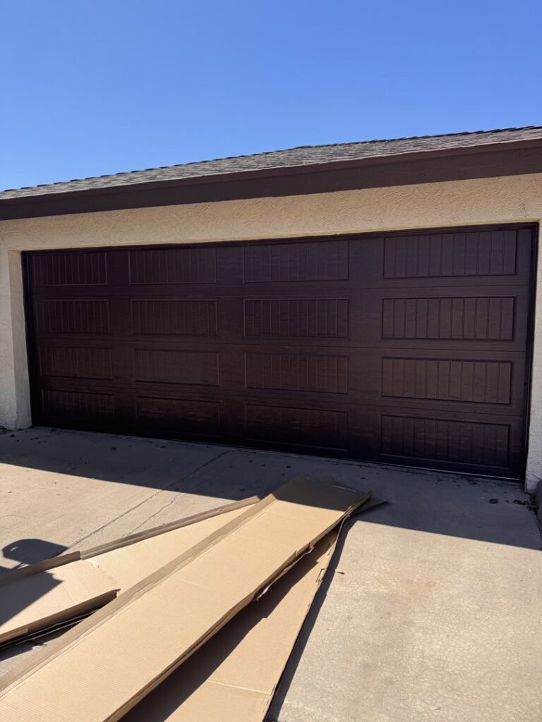 A newly installed dark brown garage door with packaging on the driveway, indicating a recent job by Gryffin Garage Door in Chandler, AZ