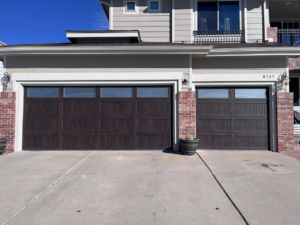 Two newly installed dark wood grain garage doors with windows on a modern home by Pham Garage Door Service & Repair in Arvada, CO.