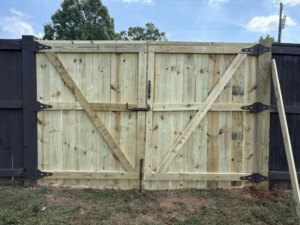 A newly installed double wooden gate with dark hardware, contrasting with the existing dark fence, by Myers & Dunlap Fence Repair in Greenville, SC.