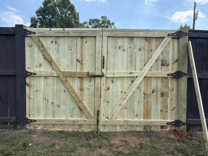 A newly installed double wooden gate with dark hardware, contrasting with the existing dark fence, by Myers & Dunlap Fence Repair in Greenville, SC.
