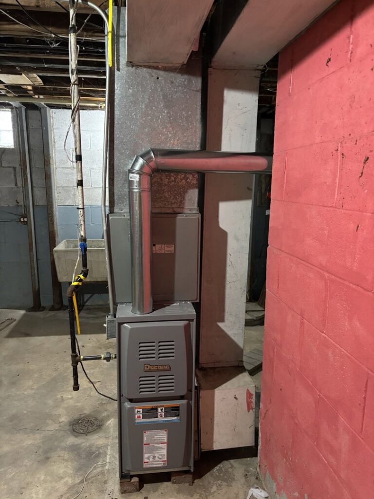 A new Ducane furnace installation next to a red painted wall in a basement by Nordic Air Heating & Cooling in West Allis, WI.