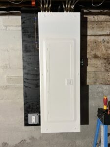 A new electrical panel and outlet installed on a black mounting board by Josh LaFerriere Electric in Westbrook, ME.